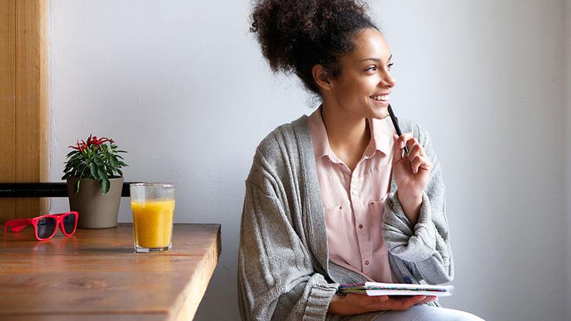 smiling African American woman writing in journal in pajamas